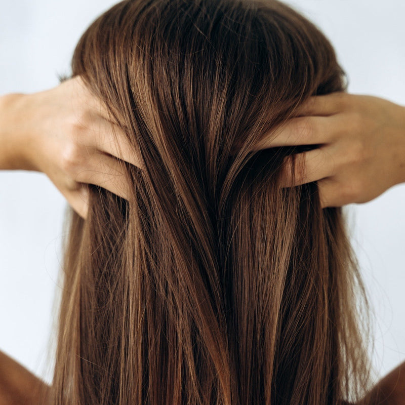 Woman running her hands through long brown hair, seen from behind